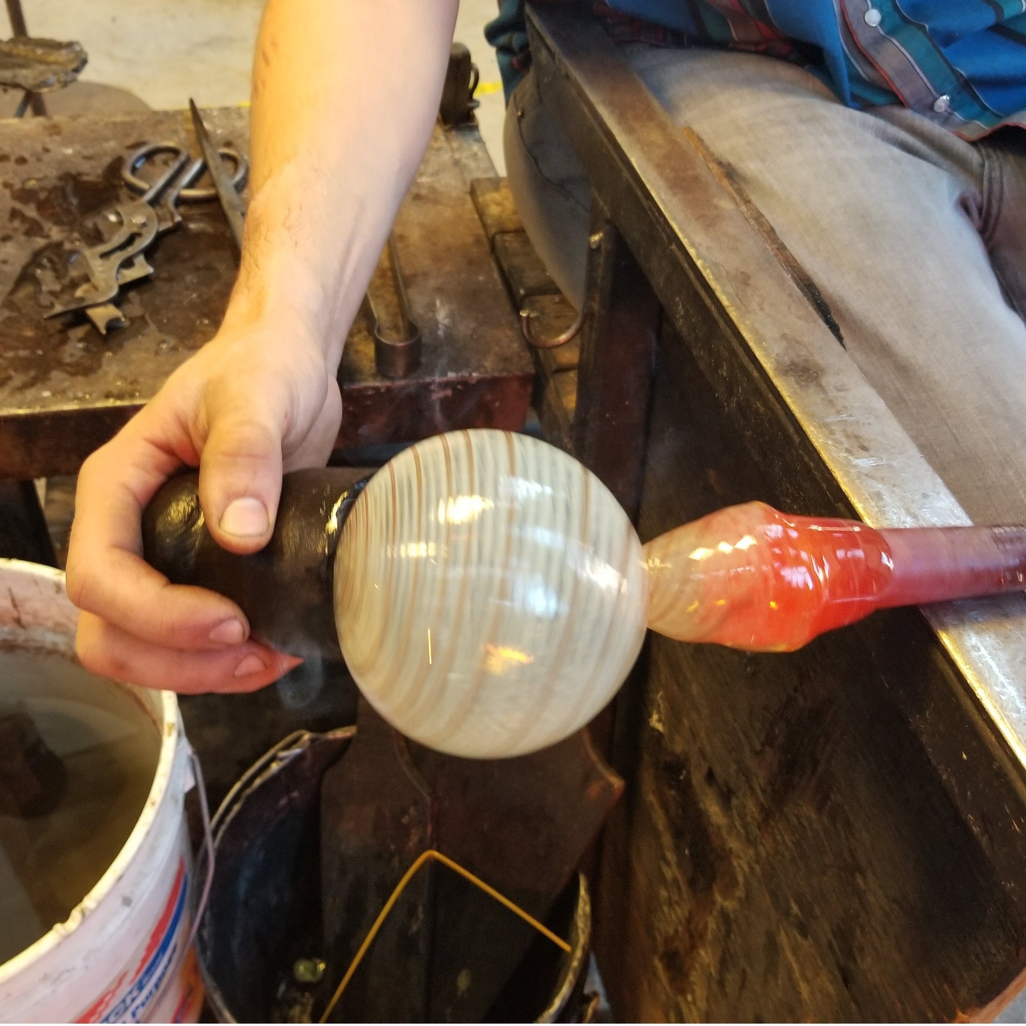 A person shaping a glass ornament on a blowpipe during a glassblowing workshop.